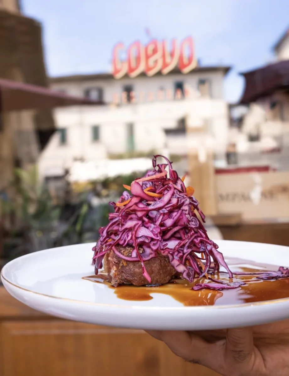 Insegna al neon del ristorante Coèvo a Pistoia con un piatto di carne servito in terrazza